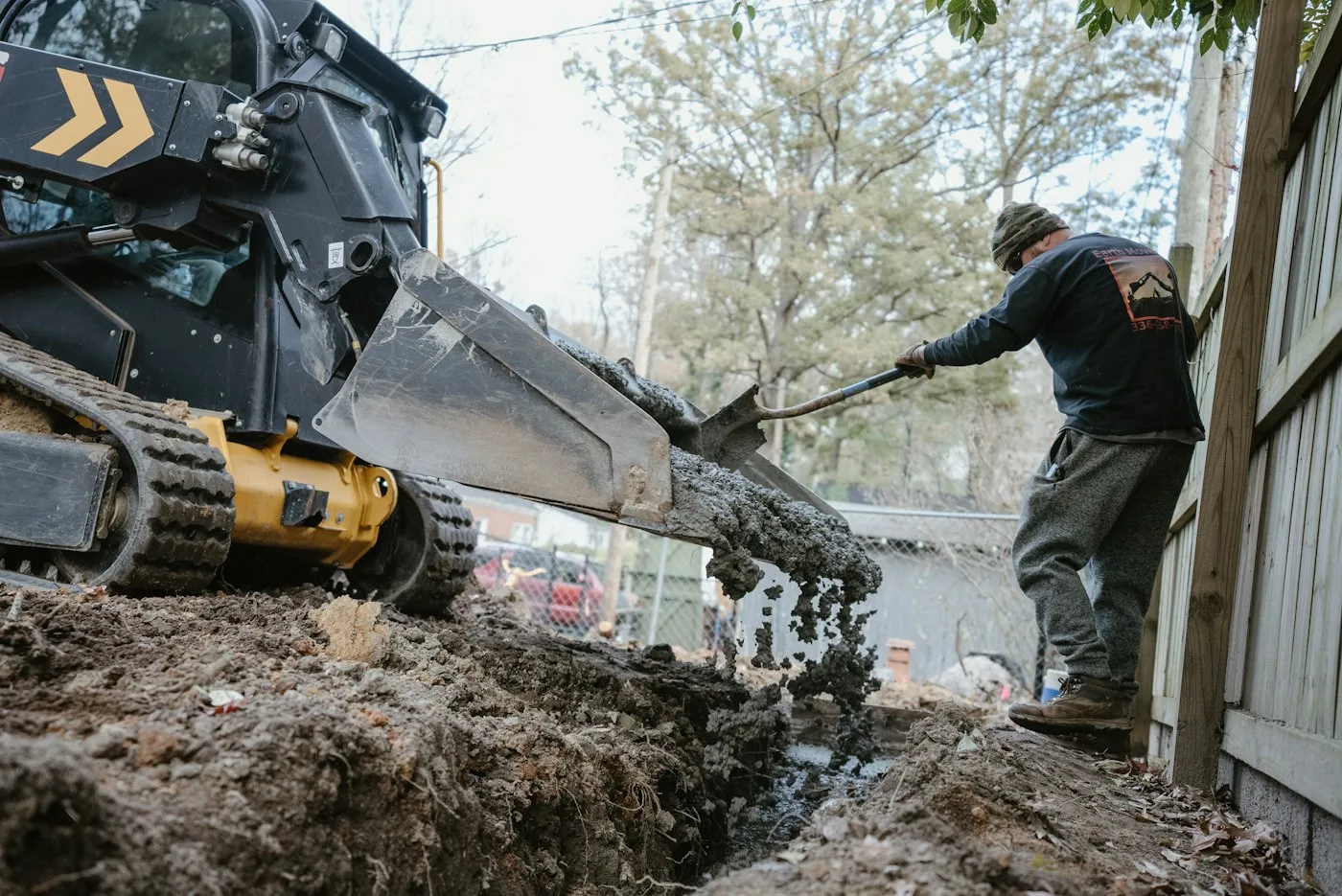 Compact loader and worker beside a residential trench